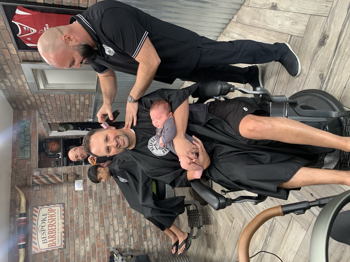 Boris cutting hair while client holds his newborn baby. Trust runs deep.